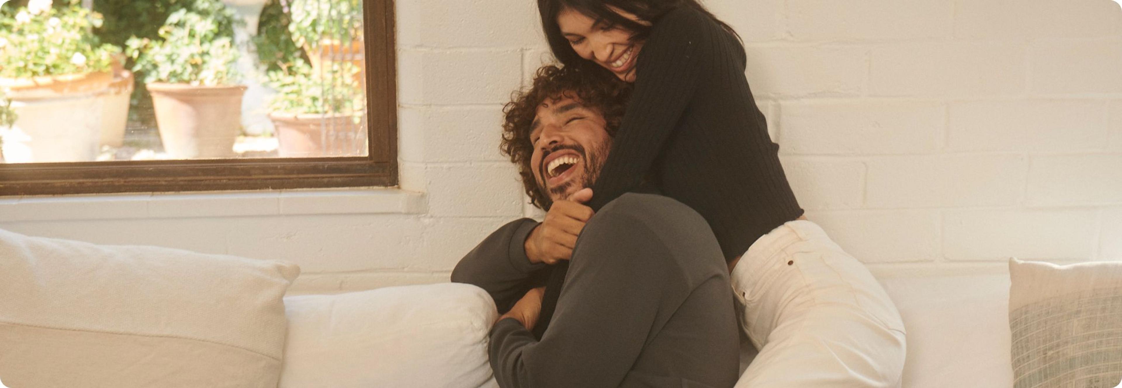  a man and a women hugging and laughing on a couch