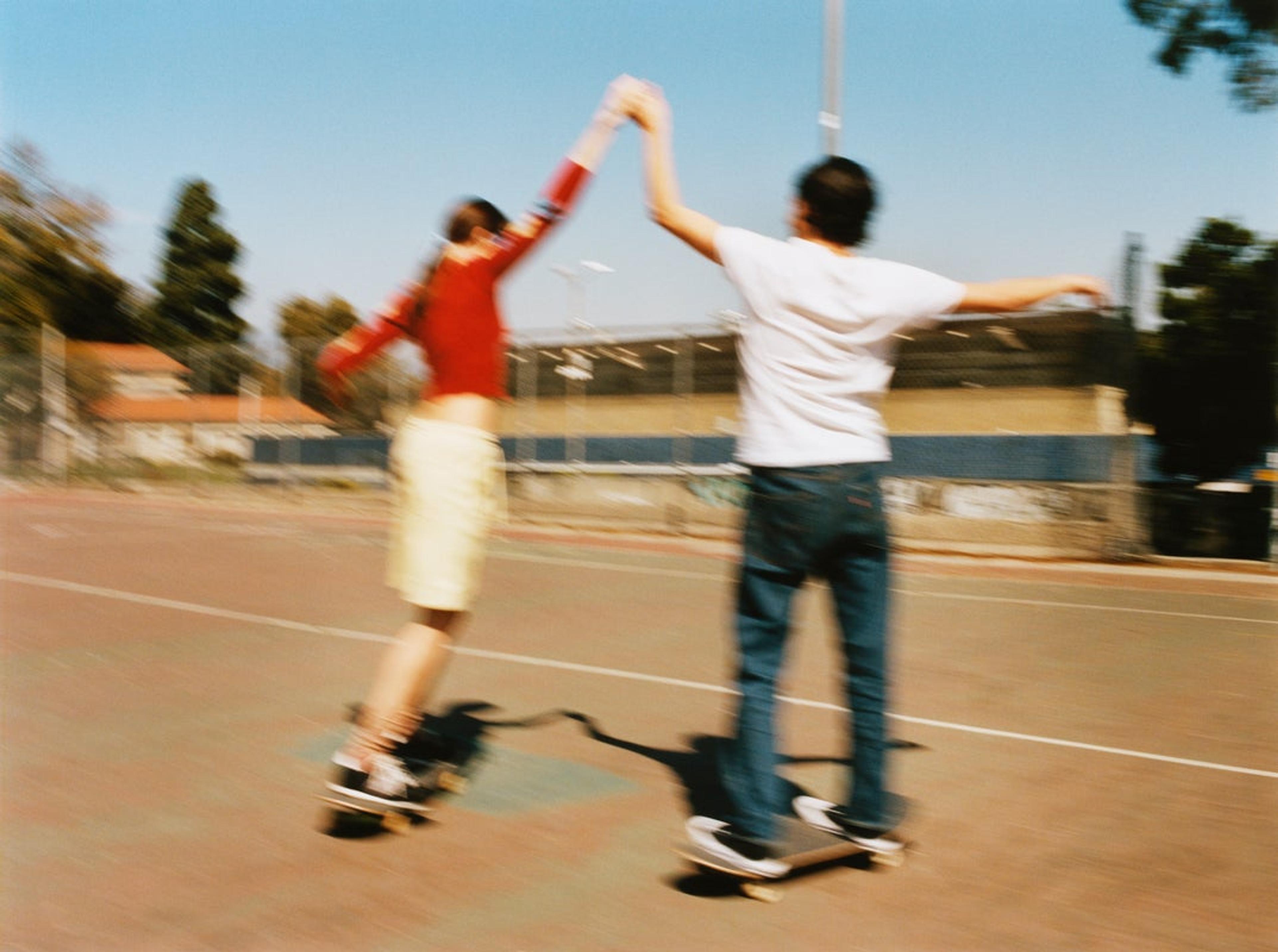 A woman and man stand on skateboards, holding hands 