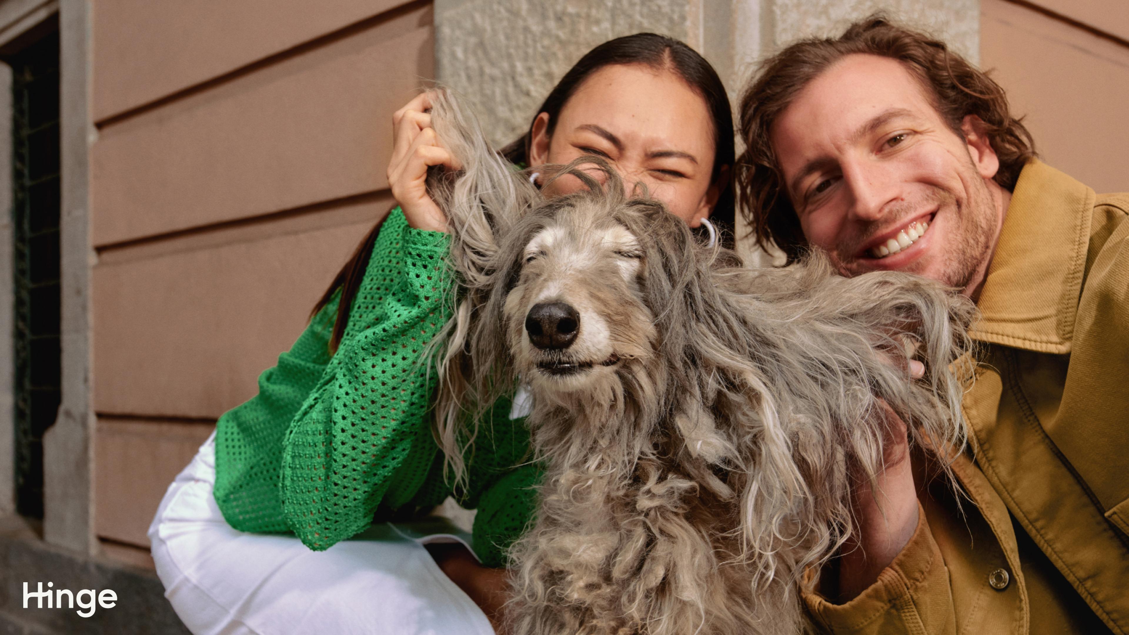 A photo of a woman and a man, smiling and posing with a fluffy dog